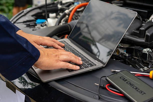 Mechanic using laptop for car diagnostics on open hood